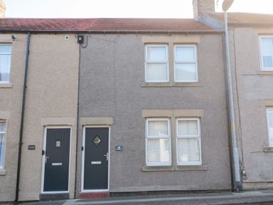 A grey two-storey terraced house with two black doors and four windows at 4 Percy Street in Amble