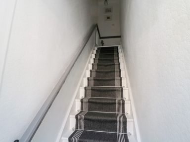 A staircase with a dark runner carpet and handrails on both sides at 4 Percy Street in Amble