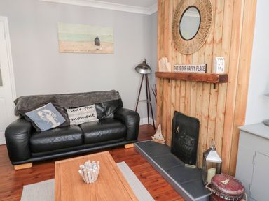 A living room with a black leather sofa cushions wooden coffee table and a fireplace with wooden paneling at 4 Percy Street in Amble