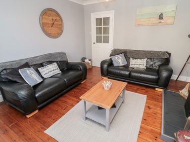 A living room with two black leather sofas a wooden coffee table on a rug and a large clock on the wall at 4 Percy Street in Amble