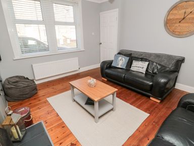 A living room with black leather sofas a wooden coffee table a large wall clock and a bean bag at 4 Percy Street in Amble