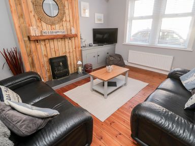 A living room with two black leather sofas a wooden coffee table on a rug a television on a cabinet and a wooden panelled fireplace at 4 Percy Street in Amble