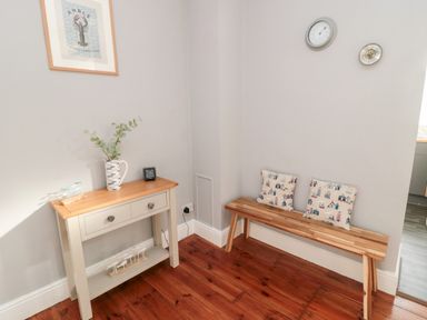 A corner with a wooden bench with two cushions and a small table with a vase and clock on it at 4 Percy Street in Amble