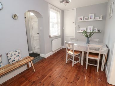 A dining area with a wooden floor and white table with chairs near a window at 4 Percy Street Amble