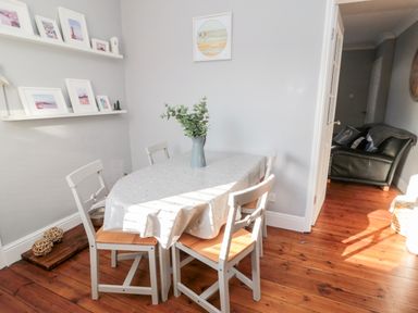 A dining area with a table covered by a tablecloth and four chairs and a vase with greenery on the table at 4 Percy Street in Amble
