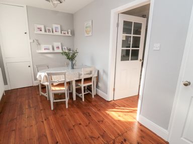 A dining area with wooden floor white table and chairs framed pictures on shelves at 4 Percy Street Amble