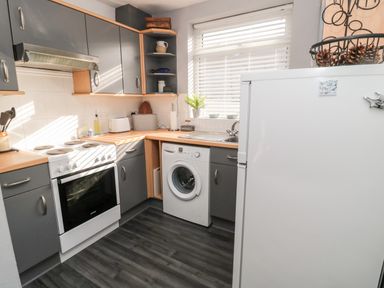 A kitchen with grey cabinets a white stove a washing machine a refrigerator and a window at 4 Percy Street in Amble