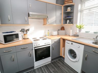 A kitchen with grey cabinets white stove microwave washing machine and a sink at 4 Percy Street in Amble