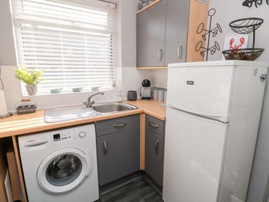 A kitchen corner with a washing machine a sink cabinets and a refrigerator at 4 Percy Street in Amble