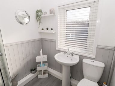 A bathroom with a toilet sink shelves and a window with blinds at 4 Percy Street in Amble