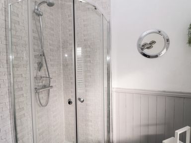A shower enclosure with glass doors and tiled walls and a round mirror on a white wall at 4 Percy Street in Amble
