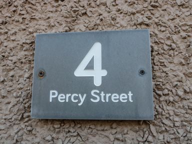 A house number sign with the number 4 and Percy Street on a textured wall at 4 Percy Street in Amble