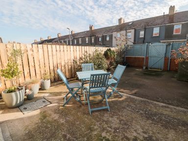 A backyard patio area with blue table and chairs potted plants and wooden fences at 4 Percy Street in Amble