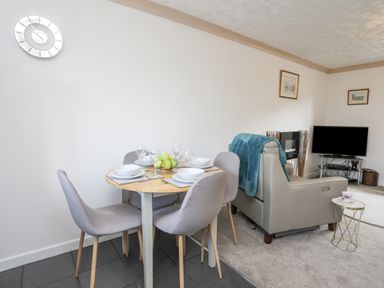 A dining table set with plates and glasses next to a living area with a sofa and television at Cae Ffynnon in Star near Gaerwen
