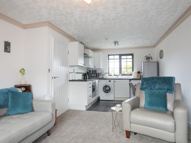 A room with a kitchen area with white cabinets and appliances and a seating area with a sofa and armchair at Cae Ffynnon in Star near Gaerwen