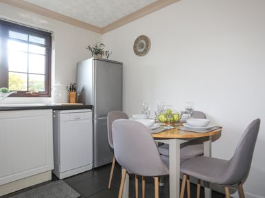 A kitchen with a dining table set with bowls and glasses and a fruit bowl with apples at Cae Ffynnon in Star near Gaerwen