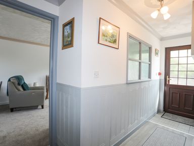 A hallway with a wooden door and framed pictures on the walls at Cae Ffynnon Star near Gaerwen