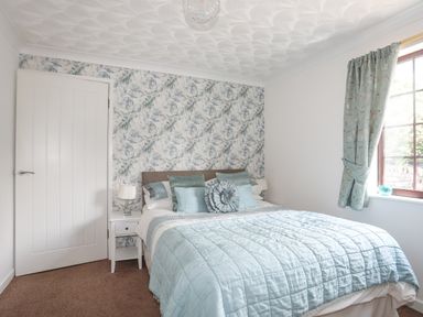 A bedroom with a bed with blue bedding and patterned wallpaper at Cae Ffynnon Star near Gaerwen
