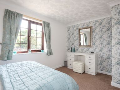 A bedroom with a bed and a window with curtains next to a dressing table with a mirror at Cae Ffynnon in Star near Gaerwen