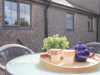 A glass outdoor table with a wooden tray holding two coffee cups a blue teapot and a small green plant at Cae Ffynnon Star near Gaerwen
