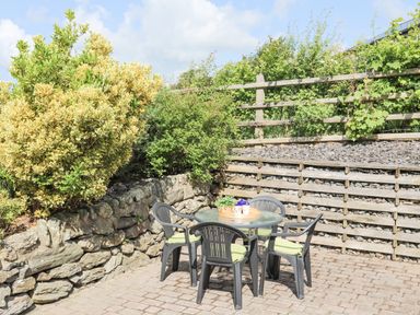 An outdoor patio area with a round table and four chairs surrounded by stone and wooden fencing at Cae Ffynnon in Star near Gaerwen