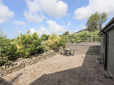 An outdoor patio area with a stone wall plants and a table with chairs at Cae Ffynnon in Star near Gaerwen