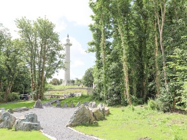 A park with a gravel path and large rocks surrounded by trees and a tall monument in the background at Cae Ffynnon in Star near Gaerwen