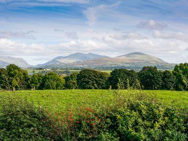 A landscape view of green fields trees and mountains under a cloudy sky at Cae Ffynnon in Star near Gaerwen