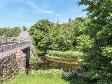 A stone bridge over a shallow river with trees and bushes surrounding it at Ty Eiddew (Ivy House) in Llanystumdwy near Criccieth