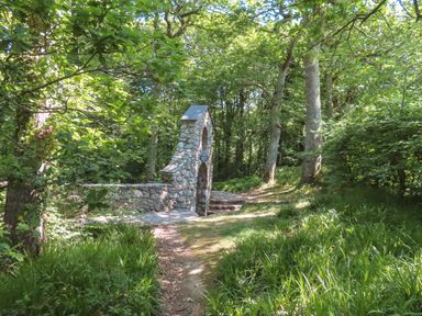 A stone monument with an arch and steps surrounded by trees and grass at Ty Eiddew Ivy House in Llanystumdwy near Criccieth