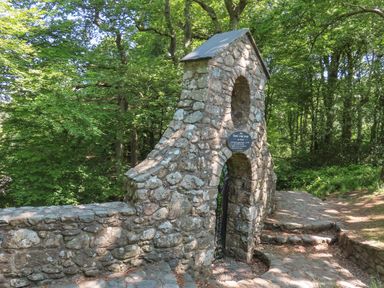 A stone archway and wall on a cobblestone path surrounded by trees at Ty Eiddew Ivy House in Llanystumdwy near Criccieth