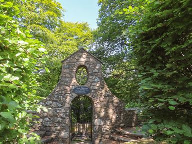 A stone archway with a metal gate surrounded by trees and greenery at Ty Eiddew Ivy House in Llanystumdwy near Criccieth