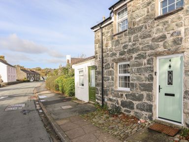 A stone house with a green door and windows next to a sidewalk along a street at Ty Eiddew Ivy House in Llanystumdwy near Criccieth