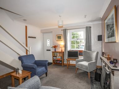 A sitting room with armchairs a small table bookshelf and a fireplace at Ty Eiddew Ivy House Llanystumdwy near Criccieth