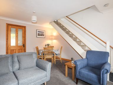 A living room with a gray sofa a blue armchair a wooden dining table and chairs under stairs at Ty Eiddew Ivy House in Llanystumdwy near Criccieth