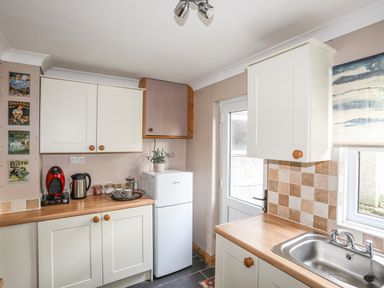 A kitchen with white cabinets a refrigerator a sink and a coffee maker at Ty Eiddew Ivy House Llanystumdwy near Criccieth