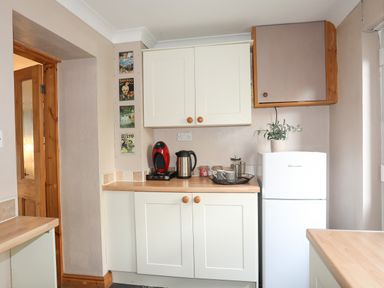 A kitchen corner with white cabinets red coffee machine kettle jars and a white fridge with a plant on top at Ty Eiddew (Ivy House) in Llanystumdwy near Criccieth