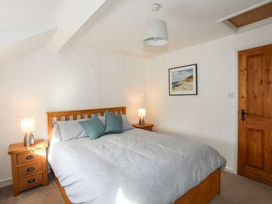 A bedroom with a double bed with gray bedding two green pillows wooden bedside tables with lamps a wooden door and a framed picture on the wall at Ty Eiddew Ivy House Llanystumdwy near Criccieth
