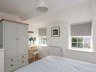 A bedroom with a bed a wardrobe a dressing table with a stool and two windows at Ty Eiddew Ivy House in Llanystumdwy near Criccieth