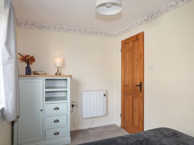 A room corner with a wooden door a white heater a light blue cabinet with a lamp books and vase on top at Ty Eiddew Ivy House Llanystumdwy near Criccieth