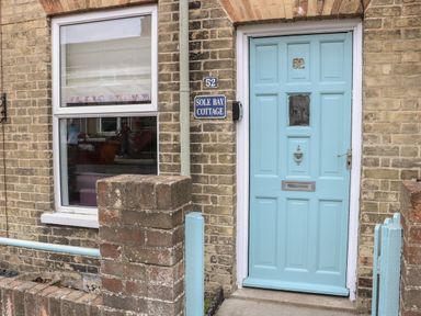 A brick cottage exterior with a blue door numbered 52 and a window next to it at Sole Bay Cottage in Lowestoft