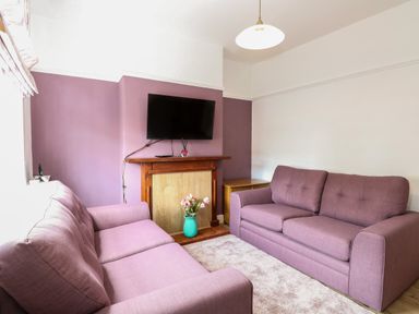 A living room with two purple sofas a wall mounted television a wooden fireplace and a vase of flowers at Sole Bay Cottage in Lowestoft