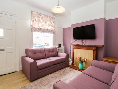 A living room with two purple sofas a wall-mounted TV and a vase with flowers at Sole Bay Cottage in Lowestoft