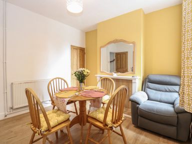 A dining area with a round wooden table and four chairs with yellow cushions and a gray armchair at Sole Bay Cottage in Lowestoft