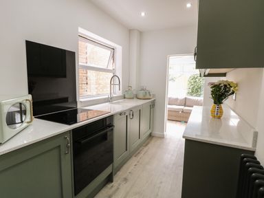 A kitchen with green cabinets a black oven a white microwave flowers in a vase and a window at Sole Bay Cottage in Lowestoft