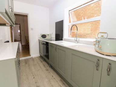 A kitchen with sage green cabinets a countertop with a toaster microwave sink and oven at Sole Bay Cottage in Lowestoft