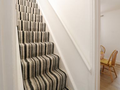 A hallway with striped carpeted stairs and a dining area with wooden chairs and a table at Sole Bay Cottage in Lowestoft