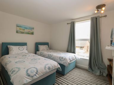 A bedroom with two single beds striped carpet and a window with curtains at Sole Bay Cottage in Lowestoft