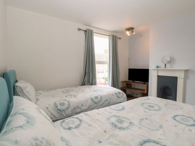 A bedroom with two beds a window curtains a fireplace with a mirror and a tv on a wooden stand at Sole Bay Cottage Lowestoft