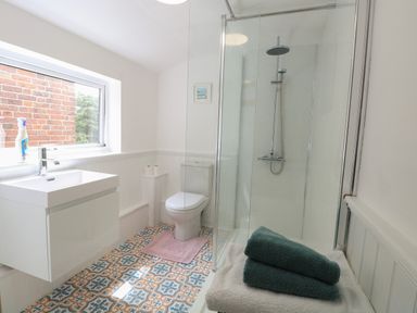 A bathroom with a sink, toilet, shower enclosure, towel rack with folded towels, and a window at Sole Bay Cottage in Lowestoft